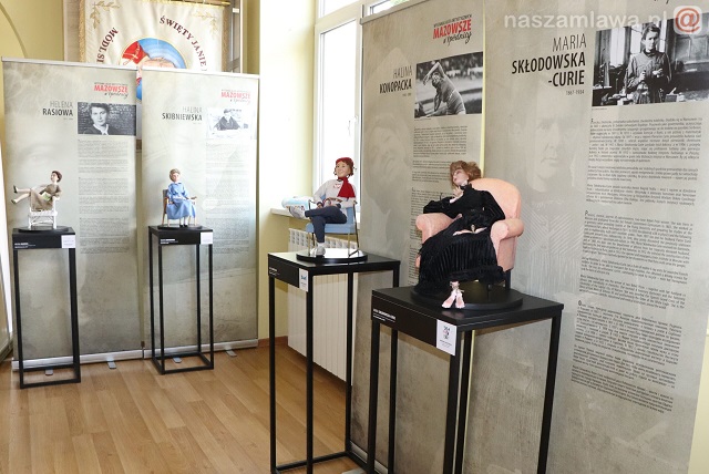 Wystawa artystycznych kalek, ekspozycja lalek na wysokich długich stołkach.